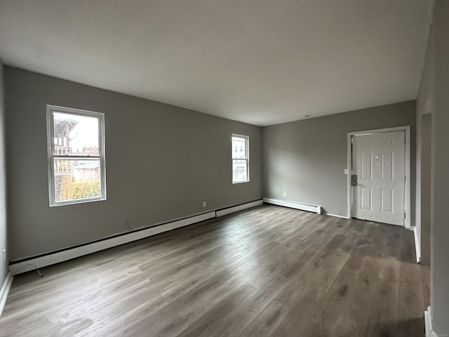 empty room featuring a baseboard radiator, baseboards, baseboard heating, and wood finished floors