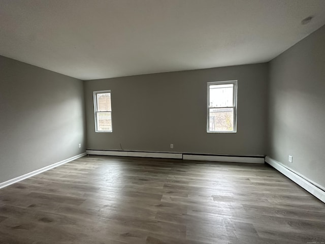 spare room with dark wood-type flooring, a baseboard heating unit, and baseboards