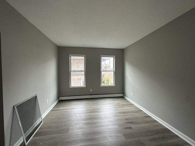 empty room featuring baseboard heating, wood finished floors, and baseboards