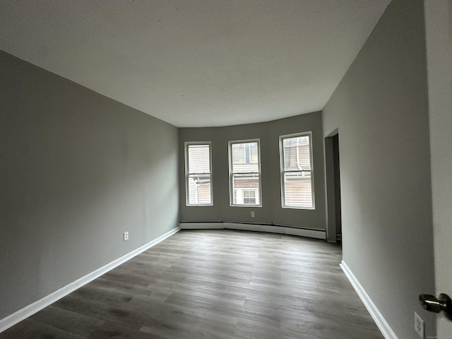 unfurnished room with baseboards, baseboard heating, and wood finished floors