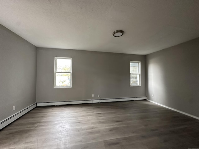 empty room featuring baseboard heating, dark wood finished floors, and a textured ceiling