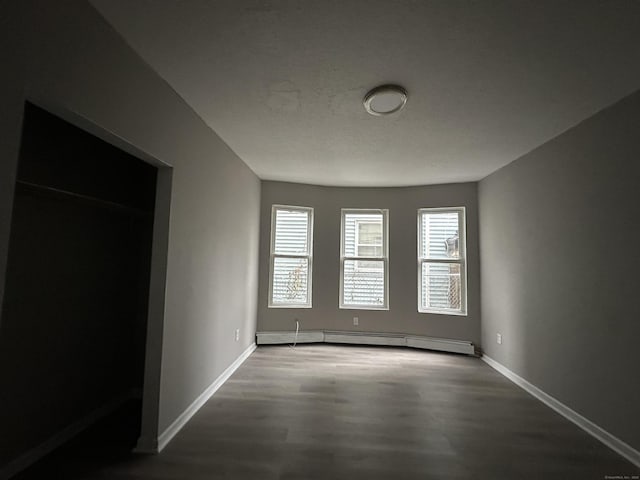 empty room featuring a baseboard radiator, wood finished floors, and baseboards