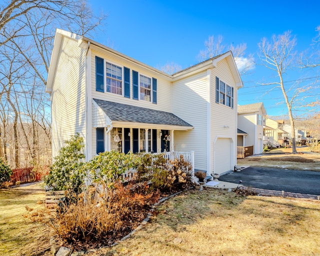 traditional home with driveway, a shingled roof, an attached garage, fence, and a porch