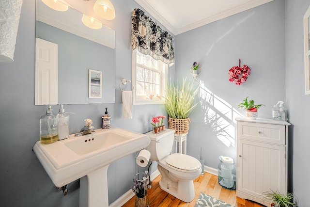 half bath with crown molding, toilet, a sink, wood finished floors, and baseboards