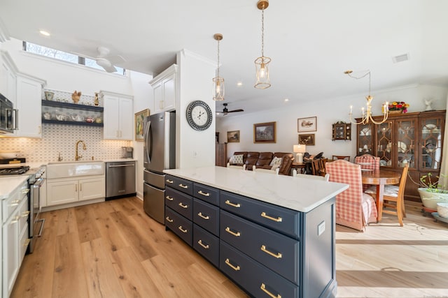 kitchen with light wood finished floors, stainless steel appliances, white cabinetry, open shelves, and ceiling fan with notable chandelier