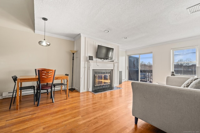 living area with visible vents, a textured ceiling, a glass covered fireplace, crown molding, and light wood-type flooring