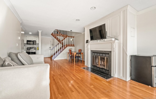 living room featuring stairway, a tile fireplace, crown molding, and light wood-style floors