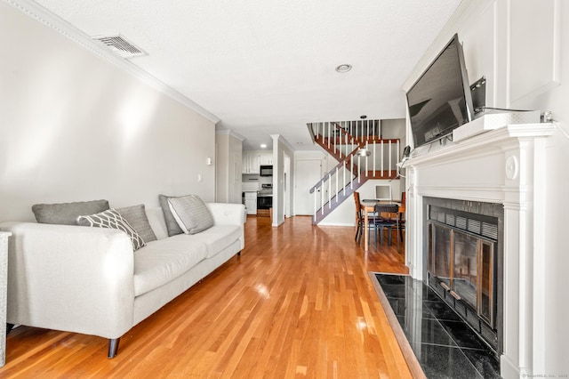 living area featuring visible vents, stairs, a tiled fireplace, crown molding, and light wood-type flooring