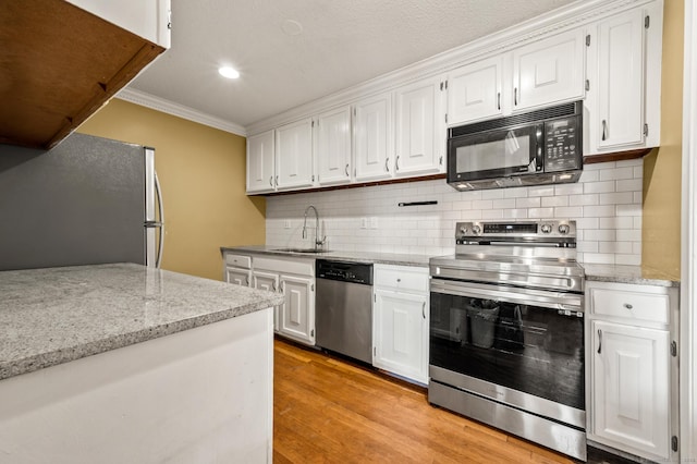 kitchen featuring light wood-type flooring, ornamental molding, appliances with stainless steel finishes, white cabinets, and a sink