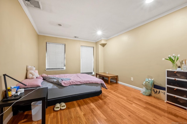 bedroom featuring baseboards, wood finished floors, visible vents, and ornamental molding