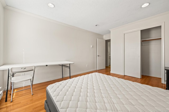 bedroom featuring baseboards, light wood-style flooring, a closet, a textured ceiling, and crown molding