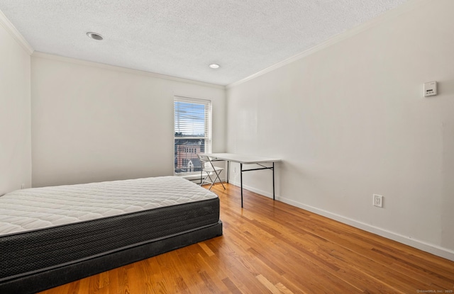 bedroom with a textured ceiling, crown molding, baseboards, and wood finished floors