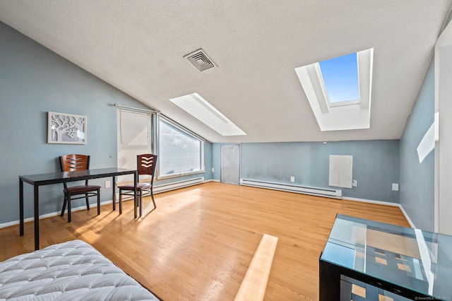 additional living space featuring visible vents, a baseboard heating unit, wood finished floors, vaulted ceiling with skylight, and baseboards