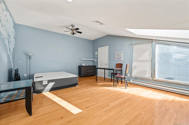 bedroom with a baseboard heating unit, vaulted ceiling with skylight, wood finished floors, and ceiling fan