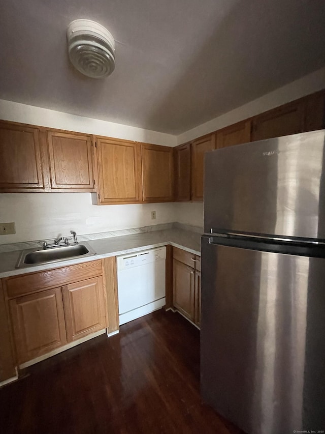 kitchen featuring white dishwasher, a sink, light countertops, freestanding refrigerator, and brown cabinetry