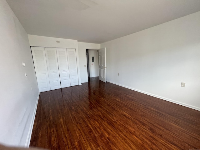 unfurnished bedroom with a closet, dark wood finished floors, and baseboards