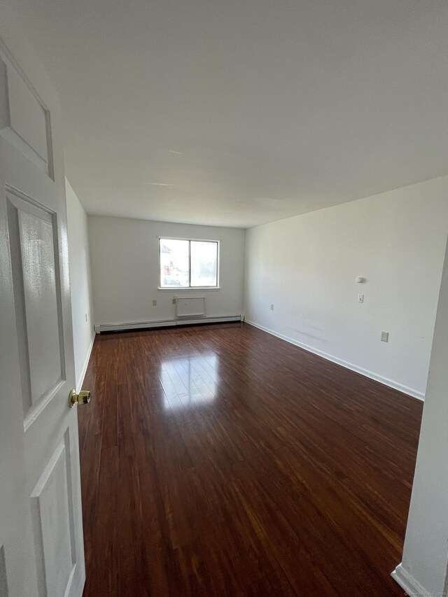 unfurnished room featuring dark wood-style floors, a baseboard heating unit, and baseboards