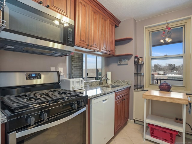 kitchen featuring stainless steel appliances, a wealth of natural light, a sink, and light stone counters