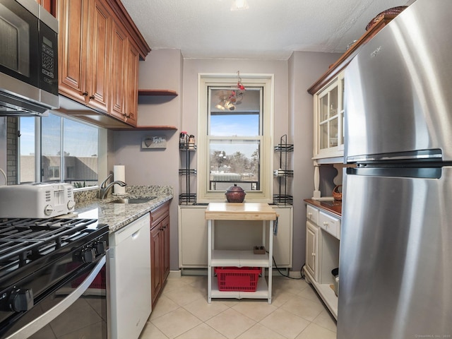 kitchen with stainless steel appliances, a healthy amount of sunlight, brown cabinetry, and a sink