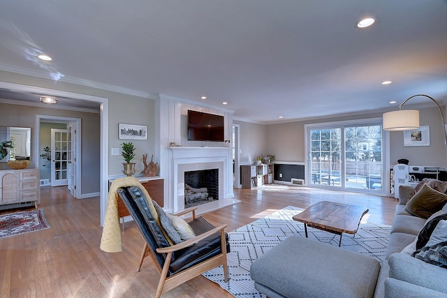 living area featuring a large fireplace, baseboards, wood finished floors, crown molding, and recessed lighting