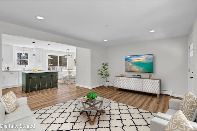 living room featuring light wood finished floors, baseboards, a baseboard heating unit, and recessed lighting