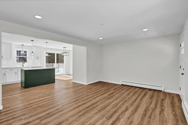 unfurnished living room featuring a baseboard radiator, a sink, baseboards, baseboard heating, and light wood finished floors