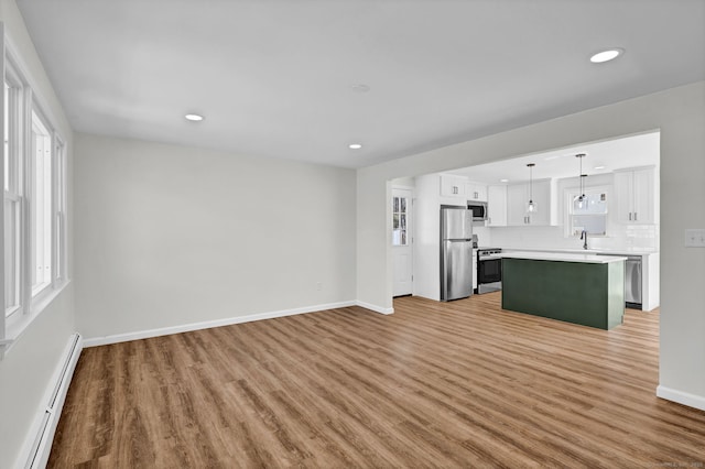 unfurnished living room featuring light wood-style floors, a baseboard radiator, baseboards, and a sink