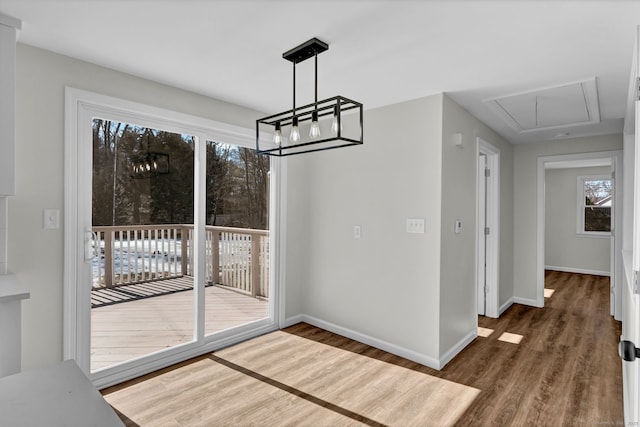 unfurnished dining area with attic access, baseboards, and wood finished floors