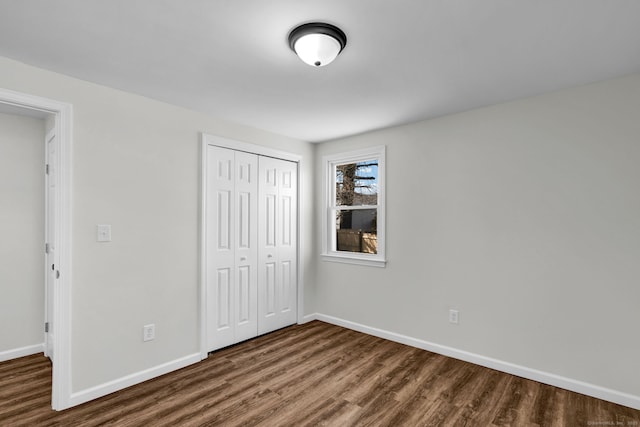 unfurnished bedroom featuring a closet, dark wood finished floors, and baseboards