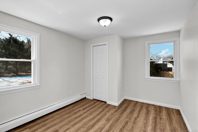 unfurnished bedroom featuring a baseboard radiator, a closet, baseboards, and wood finished floors