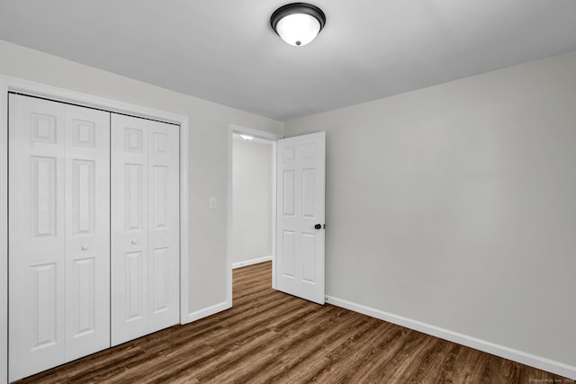 unfurnished bedroom featuring dark wood-style flooring, a closet, and baseboards