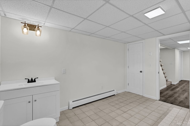 interior space featuring baseboards, baseboard heating, a drop ceiling, and vanity