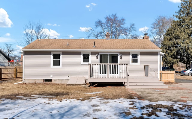 snow covered back of property featuring a chimney, roof with shingles, fence, and a deck