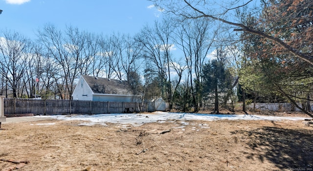 yard layered in snow featuring a storage shed, fence, and an outdoor structure