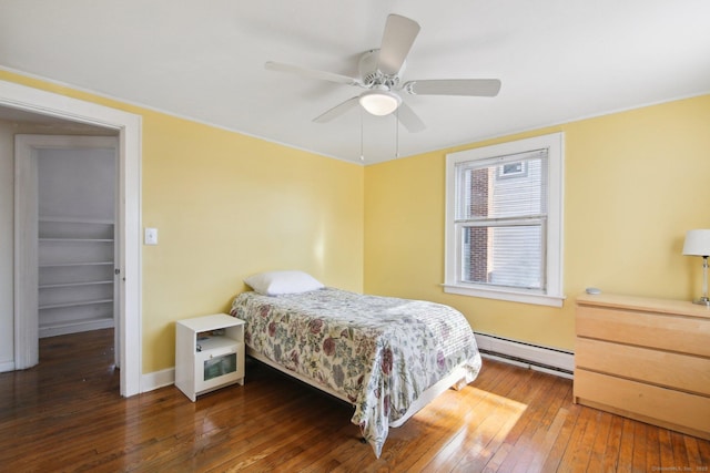 bedroom with baseboards, a ceiling fan, dark wood-style floors, a baseboard radiator, and a walk in closet