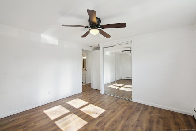 unfurnished bedroom featuring baseboards, a closet, a baseboard heating unit, and dark wood-style flooring