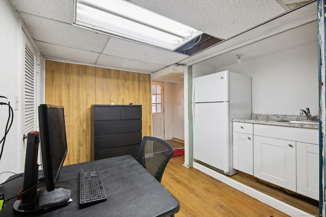 interior space with light wood-type flooring, wooden walls, and a drop ceiling