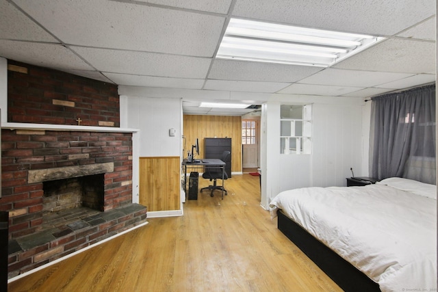 bedroom with light wood-style floors, a drop ceiling, and a fireplace