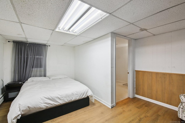 bedroom with a drop ceiling, wood walls, and wood finished floors