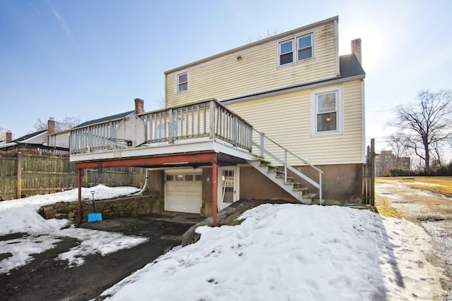 snow covered rear of property featuring an attached garage and a wooden deck