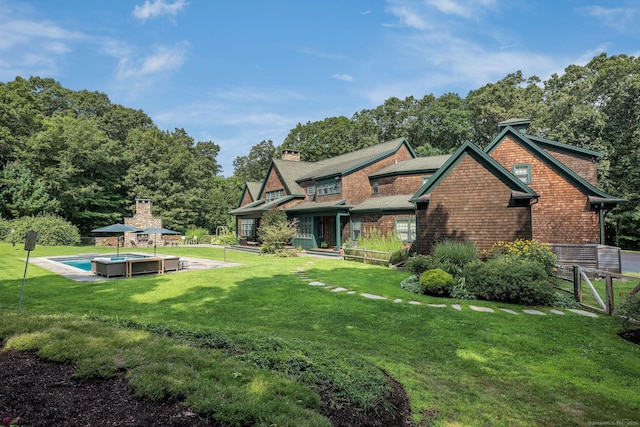 rear view of house with a chimney, fence, an outdoor pool, and a yard