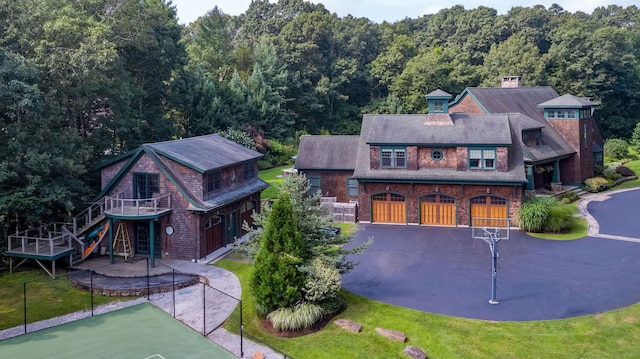 view of front of property featuring driveway, an attached garage, a front yard, a wooded view, and brick siding