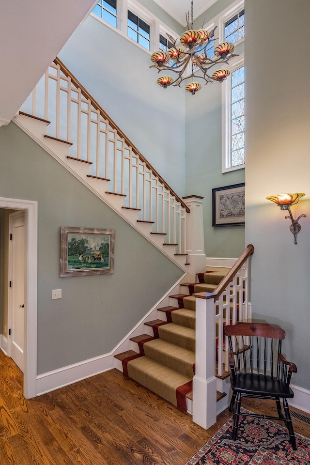 stairway with a towering ceiling, an inviting chandelier, baseboards, and wood finished floors