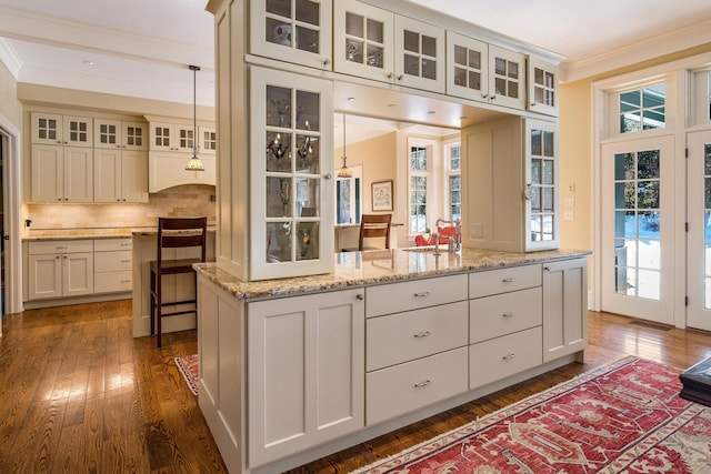 kitchen with tasteful backsplash, dark wood finished floors, light stone counters, and crown molding