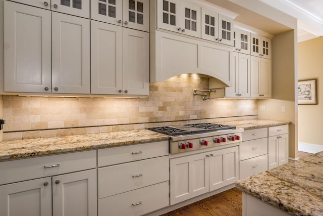 kitchen with wood finished floors, white cabinets, tasteful backsplash, glass insert cabinets, and stainless steel gas stovetop