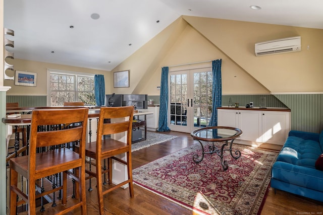 living room featuring lofted ceiling, wood finished floors, french doors, a wall mounted AC, and wainscoting