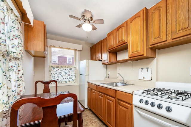 kitchen with white appliances, brown cabinetry, a ceiling fan, light countertops, and a sink