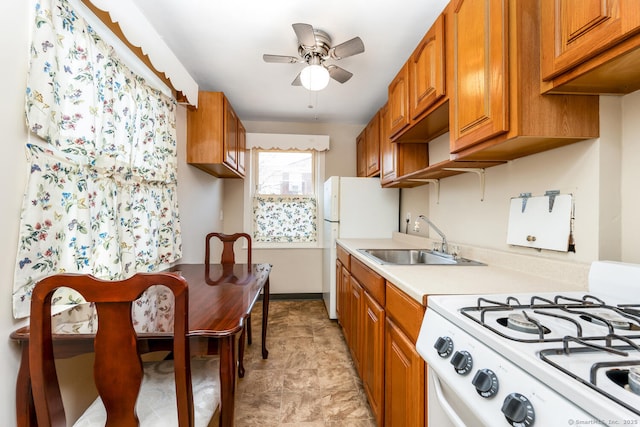 kitchen with white appliances, a sink, a ceiling fan, light countertops, and brown cabinetry