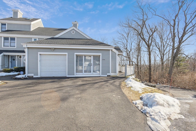 view of property exterior featuring roof with shingles, a garage, driveway, and a chimney