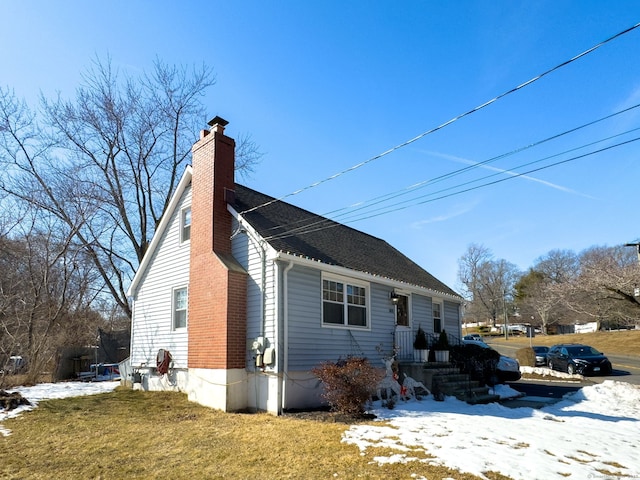 view of front of house with a shingled roof, a yard, and a chimney